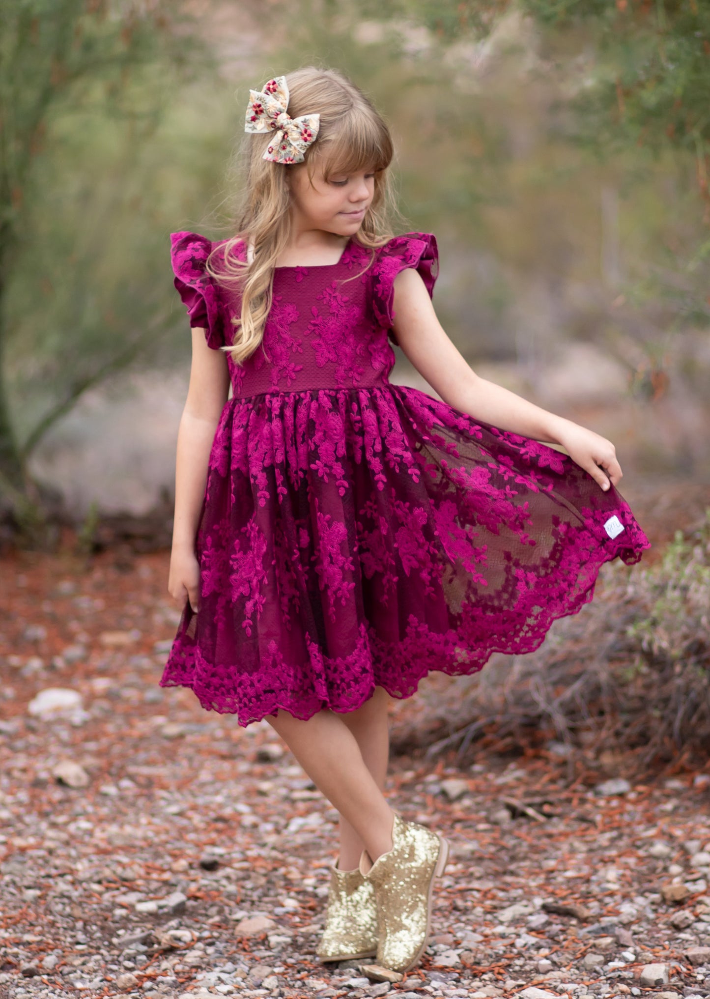 Young girl in a magenta dress with gold shoes standing in a natural setting.