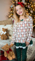 Young girl in festive pajamas holding teddy bears with Christmas decorations in the background