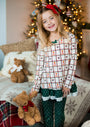 Young girl in festive pajamas holding teddy bears with Christmas decorations in the background