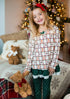 Young girl in festive pajamas holding teddy bears with Christmas decorations in the background
